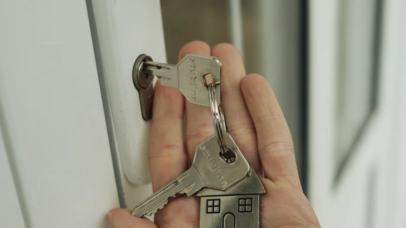 A hand holding house keys with a house-shaped keychain next to a door lock