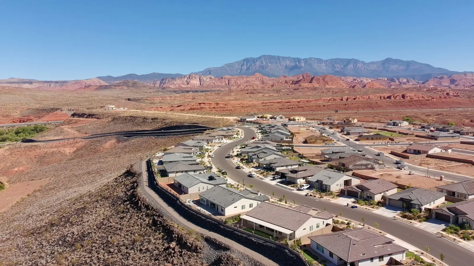 Aerial view of a new housing development curving along a desert hillside with red-rock mountains behind