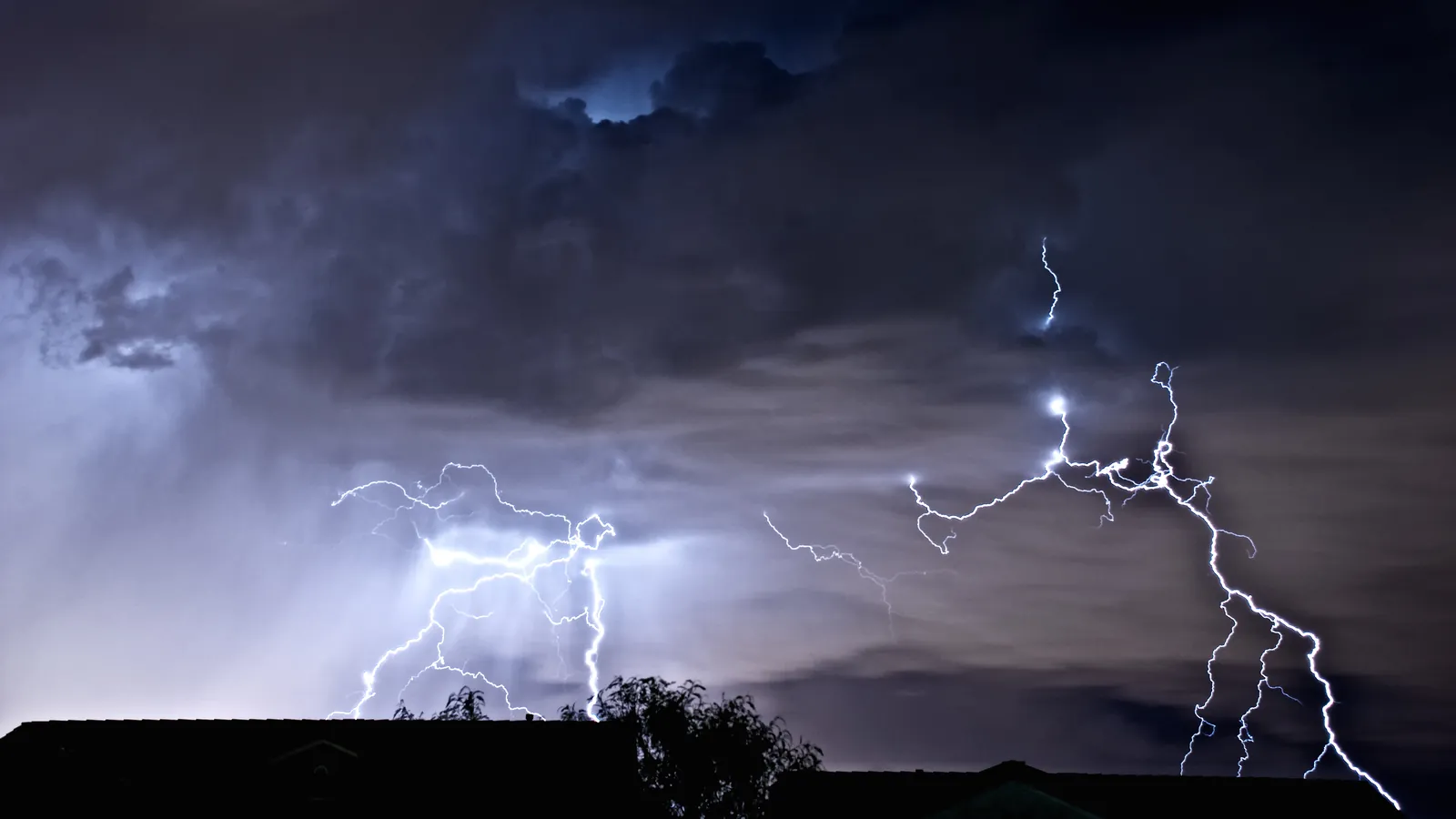 Lightning bolts from storm clouds over rooftops at night in the Las Vegas valley