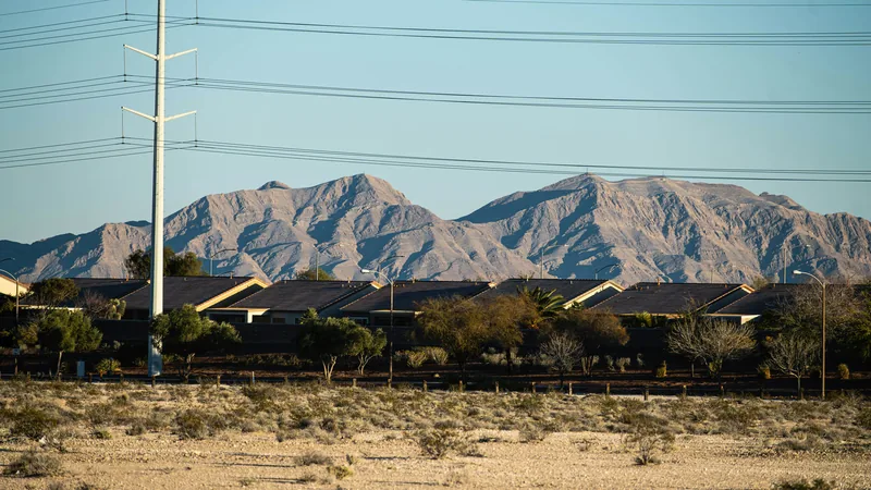 Rows of single-story houses with power lines in front of rugged desert mountains