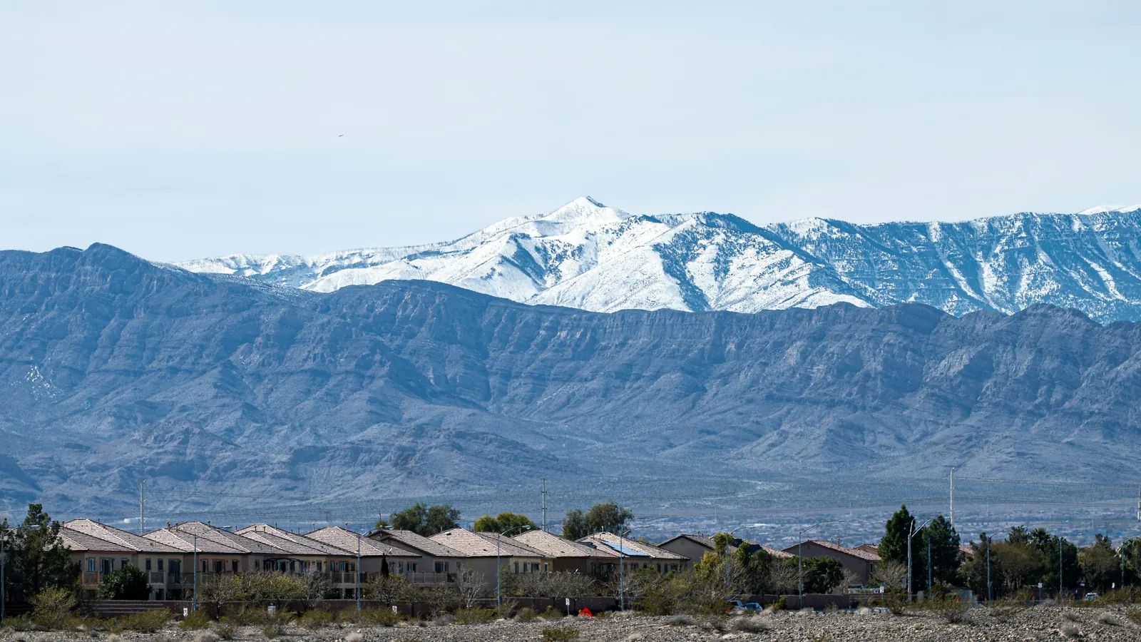 Row of houses in front of a desert valley with a snow-capped mountain range behind